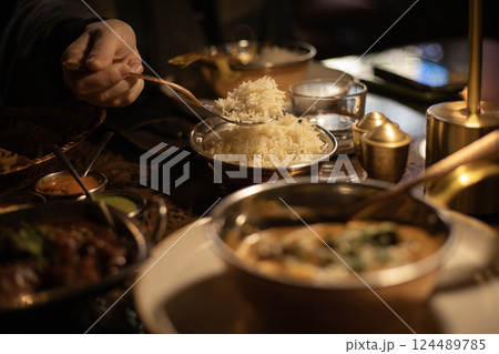 Indian dish chicken curry, in the background a man's hand is pouring rice with spoon Indian dish chicken curry, in the background a man's hand is pouring rice with spoon 124489785