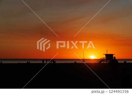 Los Angeles beach at sunset, featuring a lifeguard tower silhouette against a glowing orange and purple horizon 124491156