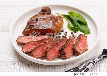 A perfectly cooked sliced striploin steak with a juicy, tender texture, served alongside a glass of rich red wine A perfectly cooked sliced striploin steak with a juicy, tender texture, served alongside a glass of rich red wine 124491190