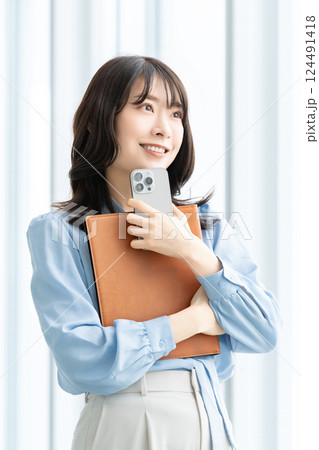 スマートフォンとバインダーを持つ笑顔の女性 スマートフォンとバインダーを持つ笑顔の女性 124491418