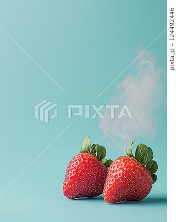 Two fresh strawberries with vibrant red color and green leaves, placed on pastel blue background, with whimsical touch of steam rising 124492446