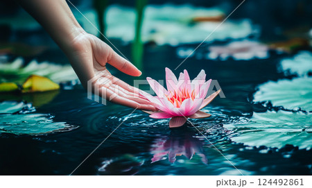 A woman's hand gently lowering delicate pink lotus flower to the surface of the water in a pond, river. Blossoming spring nature. Tranquility, harmony This is AI-generated item 124492861