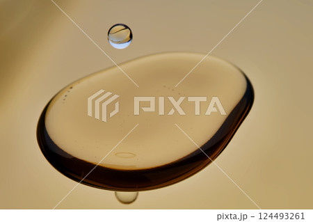 Texture of cosmetic oil with falling drop on golden background. 124493261