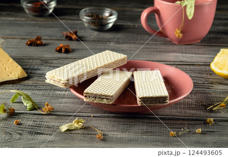 Crispy wafers are neatly arranged on a pink plate, surrounded by tea leaves, dried flowers, and a cup in a warm and inviting setting, perfect for enjoying a snack with tea Crispy wafers are neatly arranged on a pink plate, surrounded by tea leaves, dried flowers, and a cup in a warm and inviting setting, perfect for enjoying a snack with tea 124493605