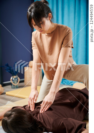 Masseuse making thai yoga massage. Woman therapist doing traditional massage treatment for female patient indoors. Client lying on mat, meditating, enjoying hand massage in calm atmosphere. Masseuse making thai yoga massage. Woman therapist doing traditional massage treatment for female patient indoors. Client lying on mat, meditating, enjoying hand massage in calm atmosphere. 124494559