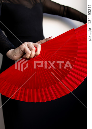 Female hand holding red fan with black dress detail Female hand holding red fan with black dress detail 124495253