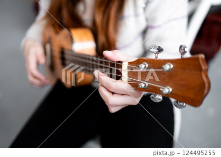 Caucasian female playing ukulele with focus on fingerpicking technique Caucasian female playing ukulele with focus on fingerpicking technique 124495255