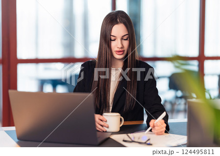Coffee, emails, deadlines. A businesswoman types on her laptop in a bright office, balancing meetings and projects. The everyday rhythm of corporate life in a digital world 124495811