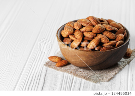 Shelled almonds are overflowing wooden bowl placed on small cloth napkin on white table, creating warm and inviting scene perfect for healthy snacking Shelled almonds are overflowing wooden bowl placed on small cloth napkin on white table, creating warm and inviting scene perfect for healthy snacking 124496034