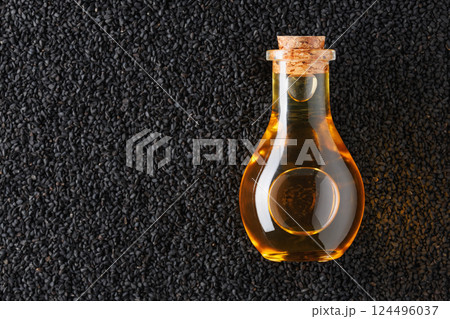 Glass bottle containing golden oil resting on bed of black cumin seeds, highlighting the rich color contrast and natural origin Glass bottle containing golden oil resting on bed of black cumin seeds, highlighting the rich color contrast and natural origin 124496037