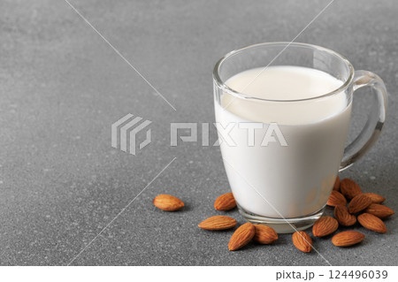 Glass cup filled with milk sits on gray background, surrounded by scattering almonds, creating visually appealing and healthy image Glass cup filled with milk sits on gray background, surrounded by scattering almonds, creating visually appealing and healthy image 124496039