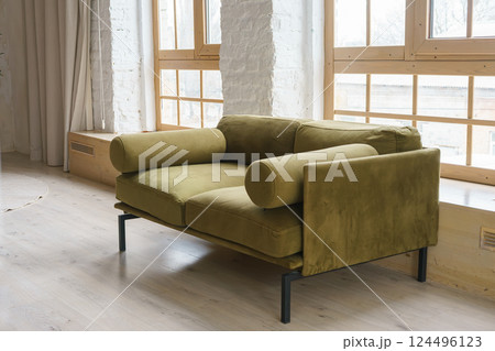 Cozy green khaki couch in bright and airy living space with large windows and brick wall backround 124496123