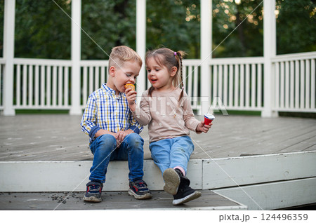 Happy Children Eating Ice Cream Outdoors on a Wooden Terrace Happy Children Eating Ice Cream Outdoors on a Wooden Terrace 124496359