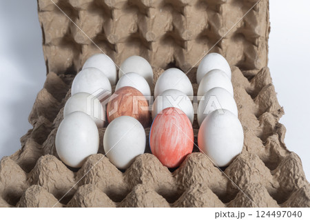 Colorful egg surrounded by plain white eggs in a cardboard box for Easter 124497040
