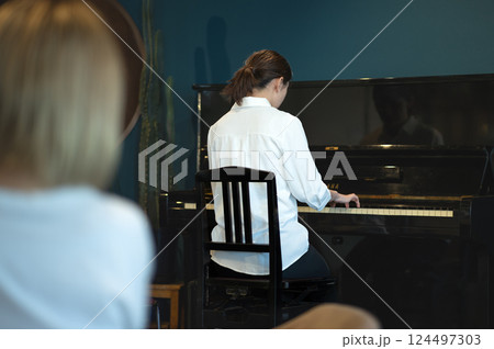 ピアノを弾く女性の後ろ姿と演奏を聴く若い女性の後ろ姿 ピアノを弾く女性の後ろ姿と演奏を聴く若い女性の後ろ姿 124497303