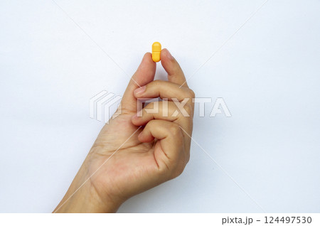 Hand holding yellow pill or capsules with customizable space for text. Medical and health matters concept 124497530