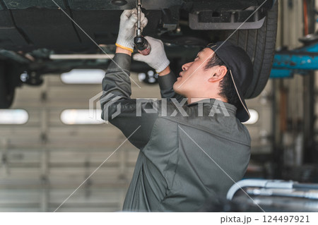 リフトで上がった車の下回りで作業・点検・整備するメカニック・整備士の男性 リフトで上がった車の下回りで作業・点検・整備するメカニック・整備士の男性 124497921