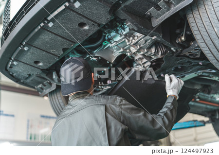 リフトで上がった車の下回りで作業・点検・整備するメカニック・整備士の男性 124497923