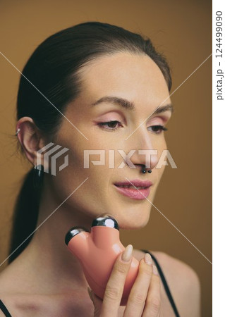 Woman using facial massage device for skincare routine at home 124499090