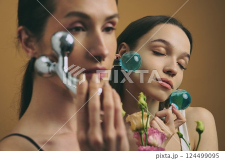 Women using facial rollers while surrounded by flowers in a serene setting Women using facial rollers while surrounded by flowers in a serene setting 124499095