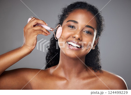 Skincare, portrait and woman with a face roller for wellness, beauty and skin routine in studio. Happy, smile and girl model from Brazil with rose quartz cosmetic tool for self care facial treatment. 124499229