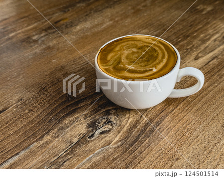 Creamy coffee resting on a rustic wooden table in morning light 124501514