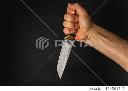 Hand holding a knife against a dark background 124501745