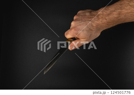 Hand holding a knife against a dark background 124501776