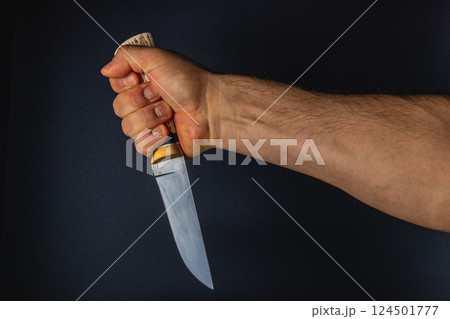 Hand gripping a knife against a dark background Hand gripping a knife against a dark background 124501777