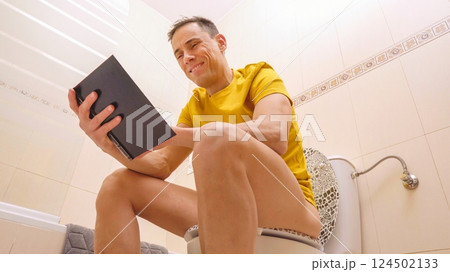 Man reading a book while sitting on the toilet Man reading a book while sitting on the toilet 124502133