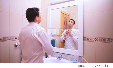 Confident businessman buttoning shirt in bathroom mirror Confident businessman buttoning shirt in bathroom mirror 124502141