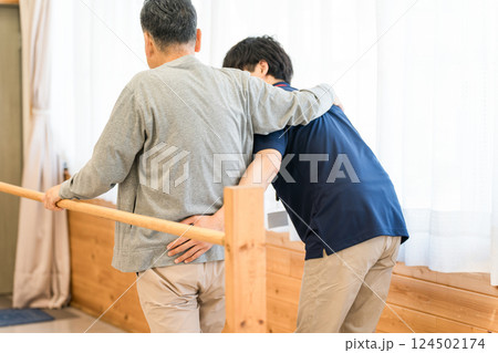 手すりを使い歩行訓練するシニア男性と介助する作業療法士,理学療法士の男性スタッフ 手すりを使い歩行訓練するシニア男性と介助する作業療法士,理学療法士の男性スタッフ 124502174