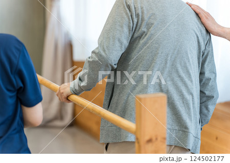 手すりを使い歩行訓練するシニア男性と介助する作業療法士,理学療法士の男性スタッフ 手すりを使い歩行訓練するシニア男性と介助する作業療法士,理学療法士の男性スタッフ 124502177