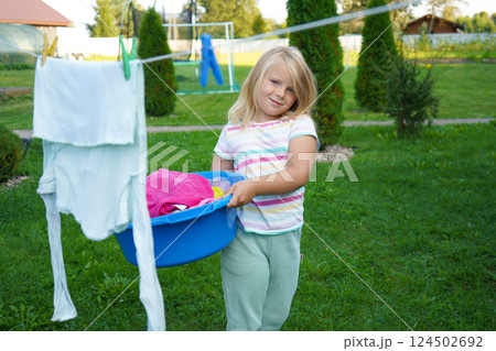 The girl, around six years old, waits near the clothesline with a plastic tub, gazing at the swaying sheets. The girl, around six years old, waits near the clothesline with a plastic tub, gazing at the swaying sheets. 124502692