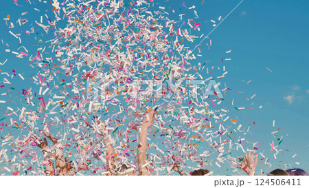 Excited students happily tossing bright confetti into the air to celebrate their graduation on a sunny summer day 124506411