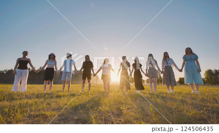 Young students linking hands in a field, savoring the summer sunset during a break 124506435