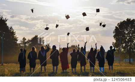 Students in academic gowns tossing graduation caps in the air at sunset to celebrate their achievement Students in academic gowns tossing graduation caps in the air at sunset to celebrate their achievement 124506483