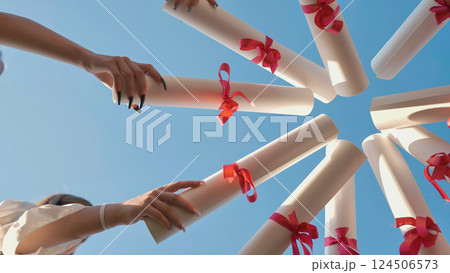 Students celebrating their graduation by raising their diplomas together under a clear blue summer sky 124506573