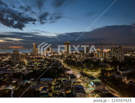 Evening skyline of a bustling coastal city with ships on the horizon during sunset Evening skyline of a bustling coastal city with ships on the horizon during sunset 124507425