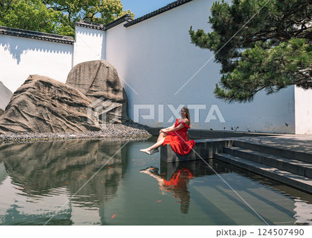 Woman in red dress relaxing by serene water in a tranquil garden in summer 124507490