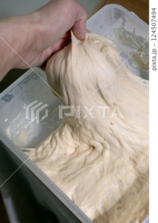 Hand Stretching Dough In Container 124507494