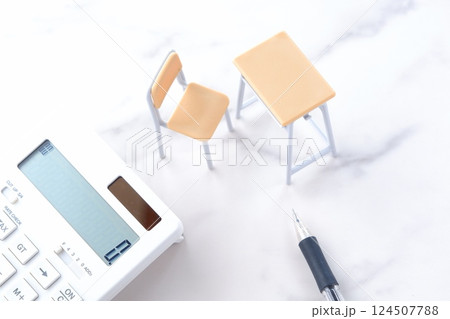 学校の机と椅子、電卓がイメージする、高騰を続けて家計を圧迫する教育費のイメージ 124507788