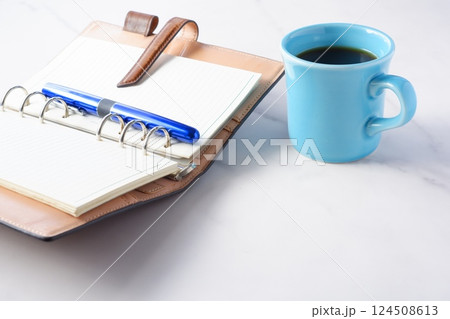 淹れたてのコーヒーを飲みながら、リング式のシステム手帳を開いてデスクワークをしているイメージ 124508613