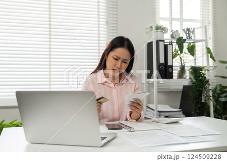 Home Office and Spending Analysis. A woman assesses her bills and expenses at home, feeling the weight of financial decisions in her workspace. 124509228