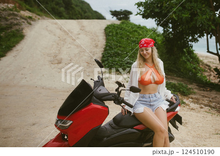Attractive caucasian woman in a bikini swimsuit on a bike scooter near the beach in sunny weather. 124510190