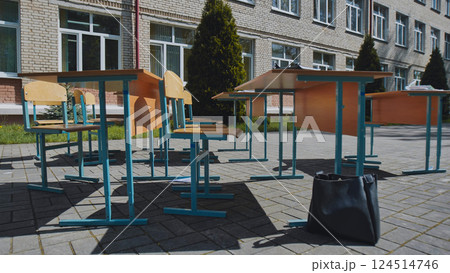 Deserted school desks and chairs set up outside school building, hinting at outdoor learning during pandemic 124514746