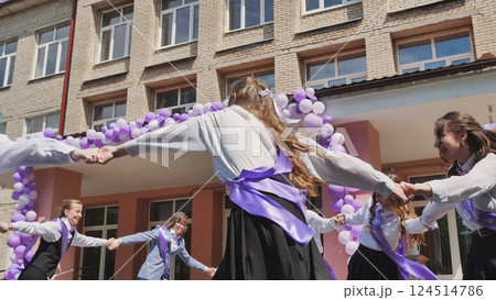 Students joyfully dancing in a circle, marking their last day of school with purple and white balloons and ribbons Students joyfully dancing in a circle, marking their last day of school with purple and white balloons and ribbons 124514786