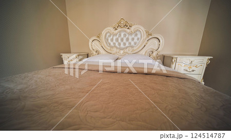 Luxurious beige king size bed with an ornate headboard, pristine white pillows, and matching nightstands, creating a romantic ambiance 124514787