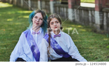 Two happy graduates celebrating their last school day, sitting on the grass in the schoolyard, wearing sashes and enjoying the moment as friends and classmates Two happy graduates celebrating their last school day, sitting on the grass in the schoolyard, wearing sashes and enjoying the moment as friends and classmates 124514800