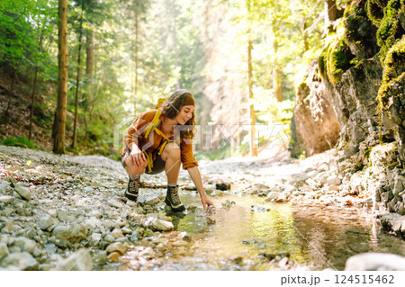 Woman traveler collects water from a stream, climbs up the mountains along a forest hiking trail. Woman traveler collects water from a stream, climbs up the mountains along a forest hiking trail. 124515462